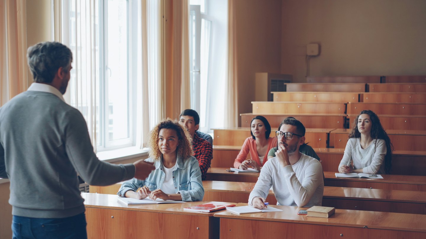 Instructor speaking to attentive college students in a lecture hall.